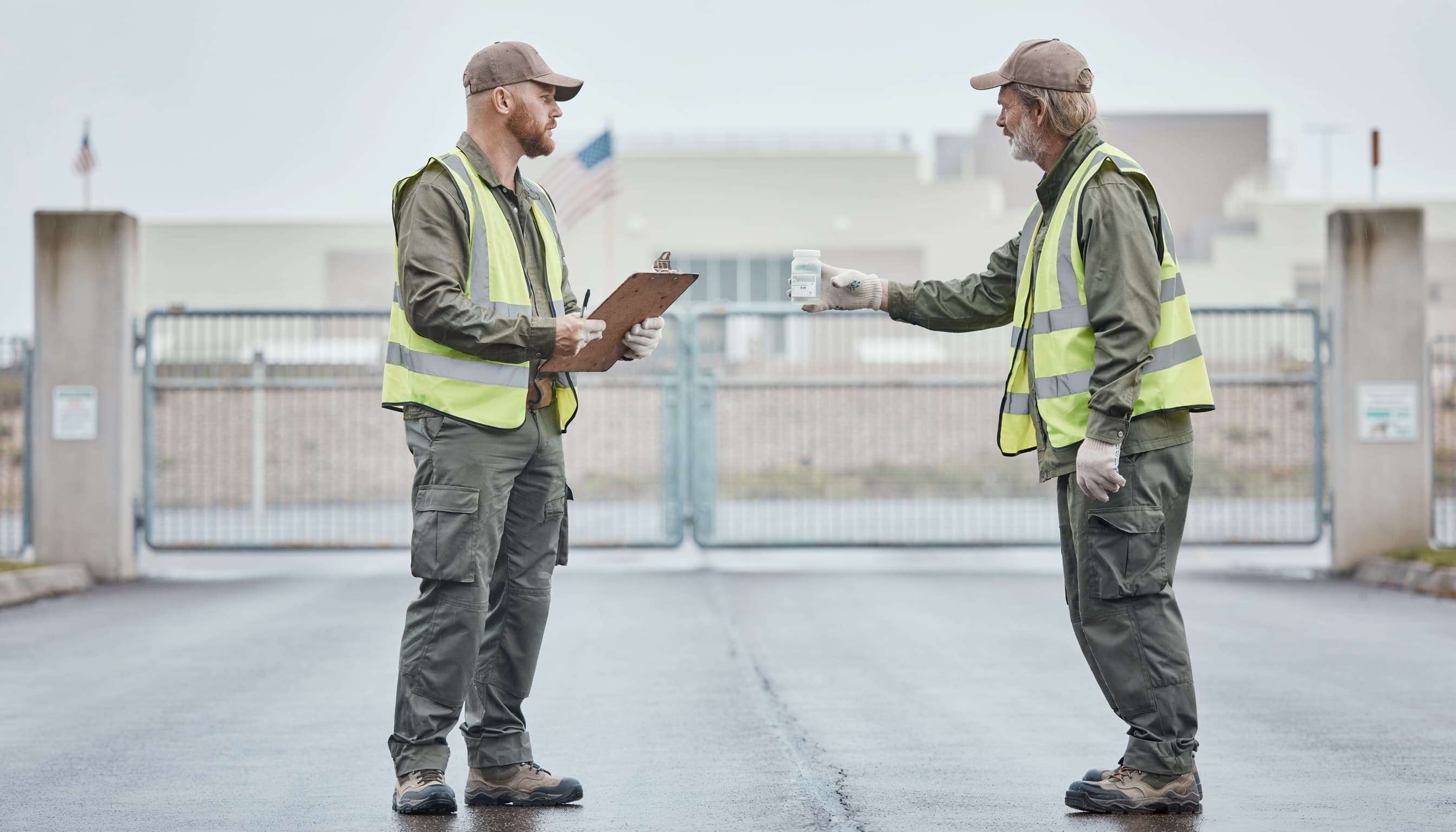 Two-person environmental field crew at a federal facility entrance gate, conducting a site assessment.